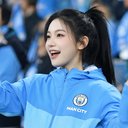 一位年轻女性球迷，扎马尾，穿着曼城外套